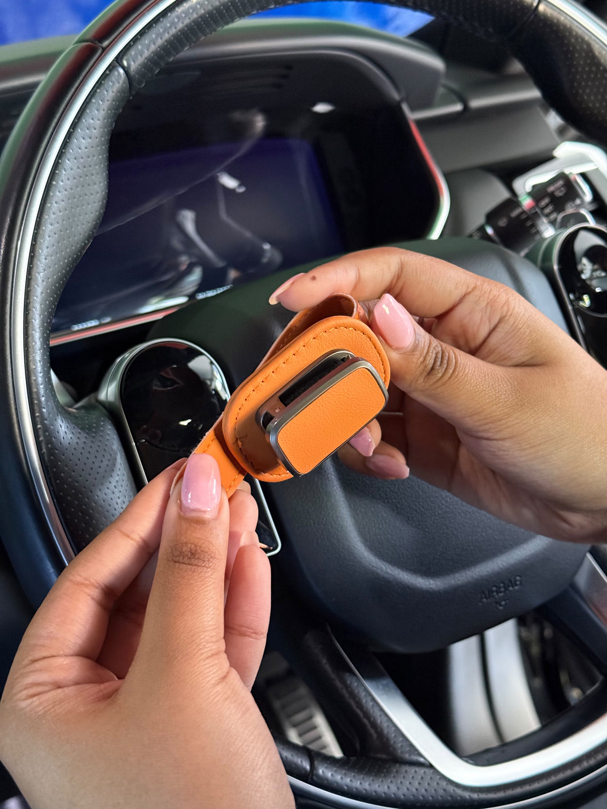Hands opening the tan Visor Clip inside a car, showing the sprung metal jaw