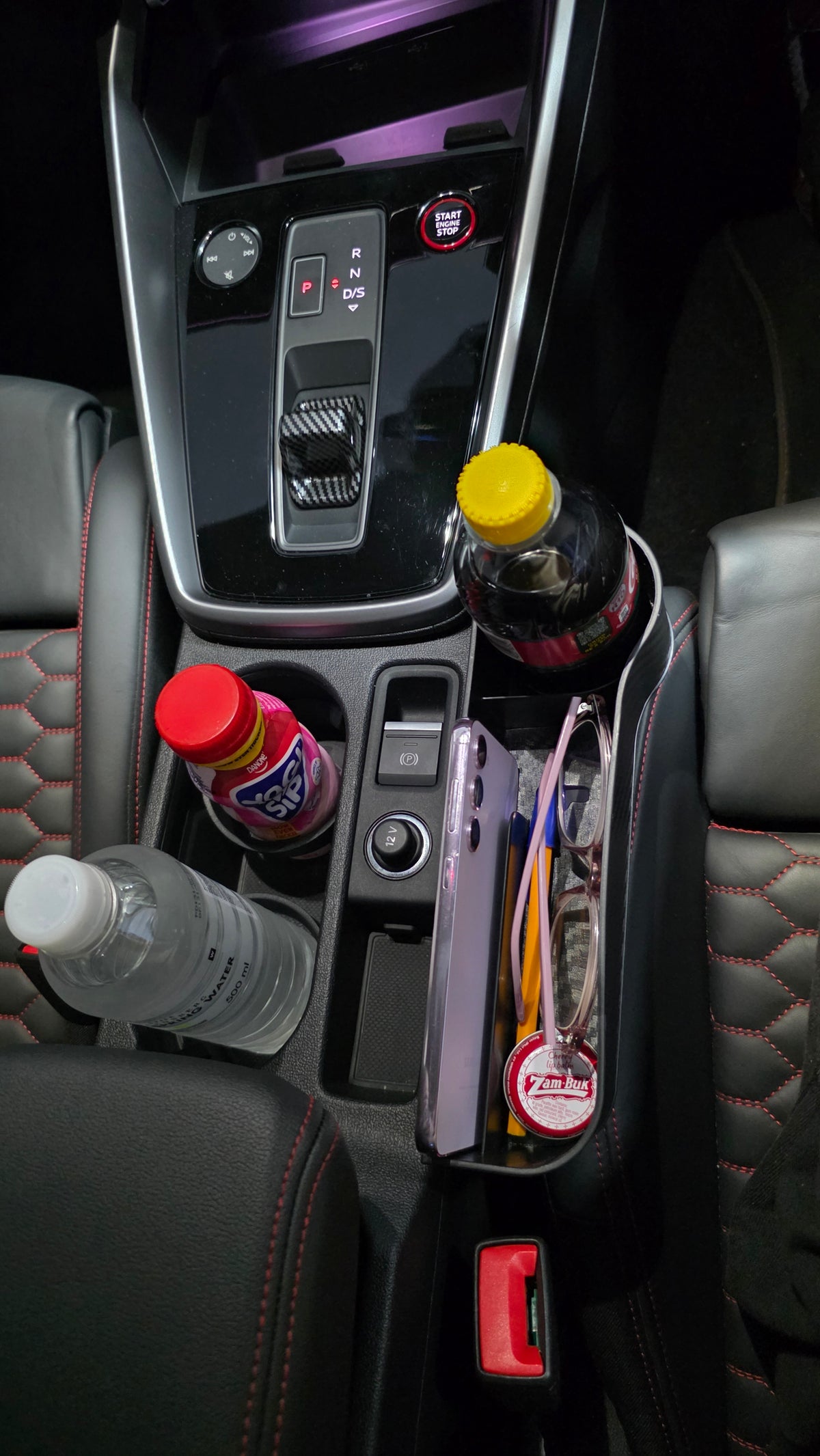 The Gap Keeper fitted beside the centre console, holding a phone upright in the built-in phone holder, glasses, pens and lip balm in the storage compartment and a drink in the cup holder