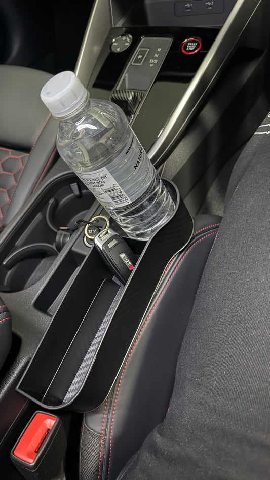 The Car Edit Gap Keeper fitted in the seat gap of a car, holding a water bottle in the cup holder and keys in the tray