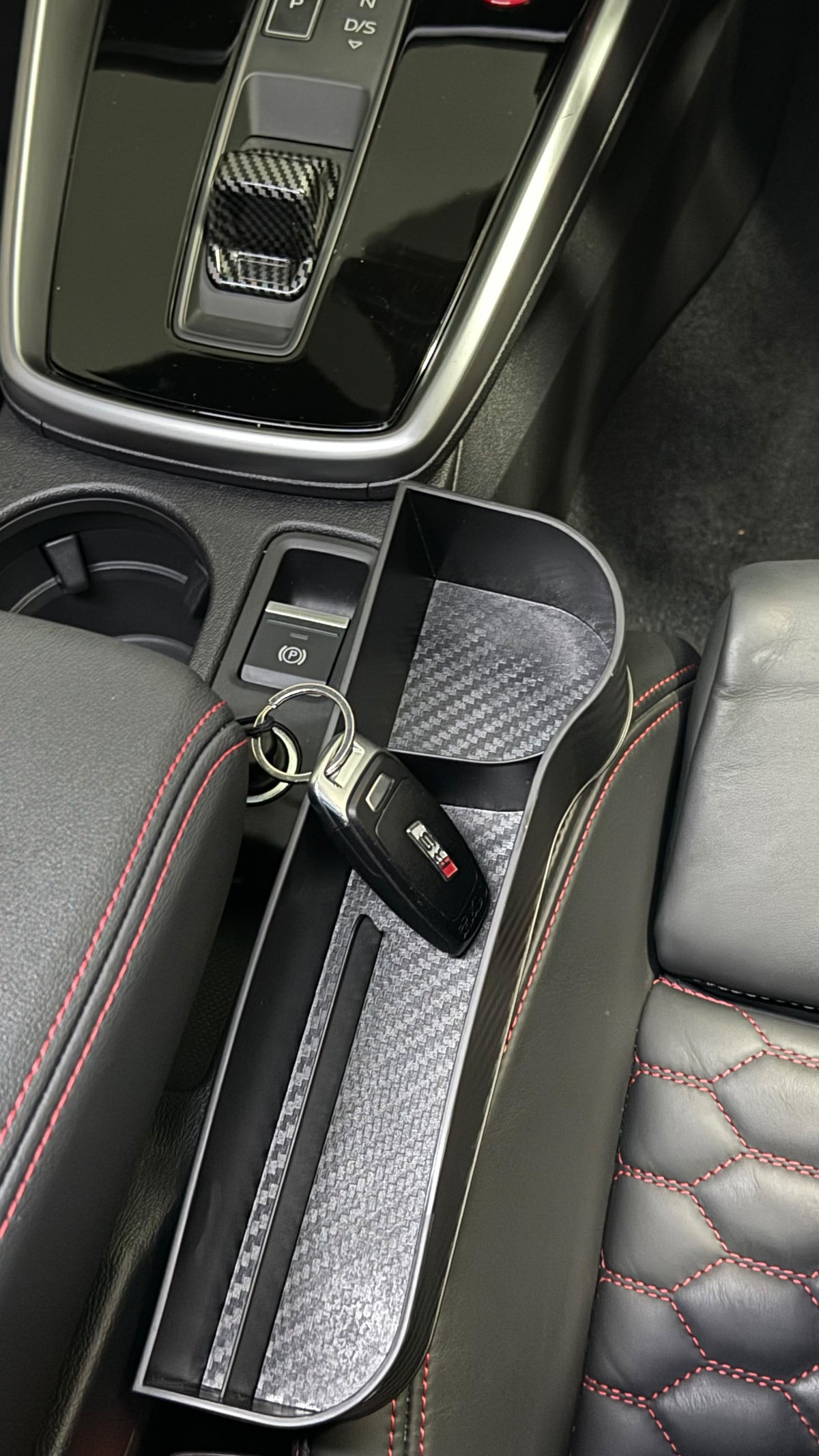 Carbon-fibre finish seat gap organiser wedged beside the centre console, holding car keys within reach of the driver