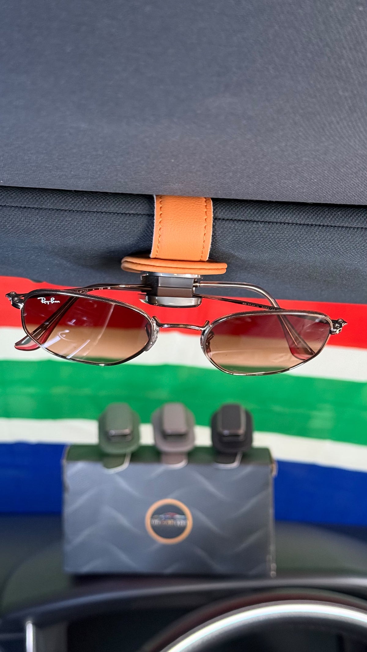 Tan leather Visor Clip holding a pair of sunglasses on a car sun visor