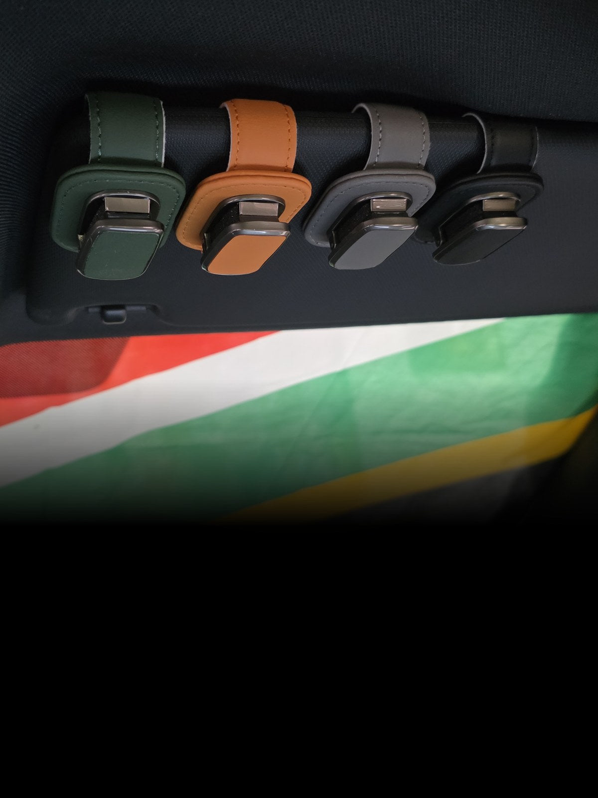 The Car Edit Visor Clip in green, tan, grey and black leather, clipped to a car sun visor